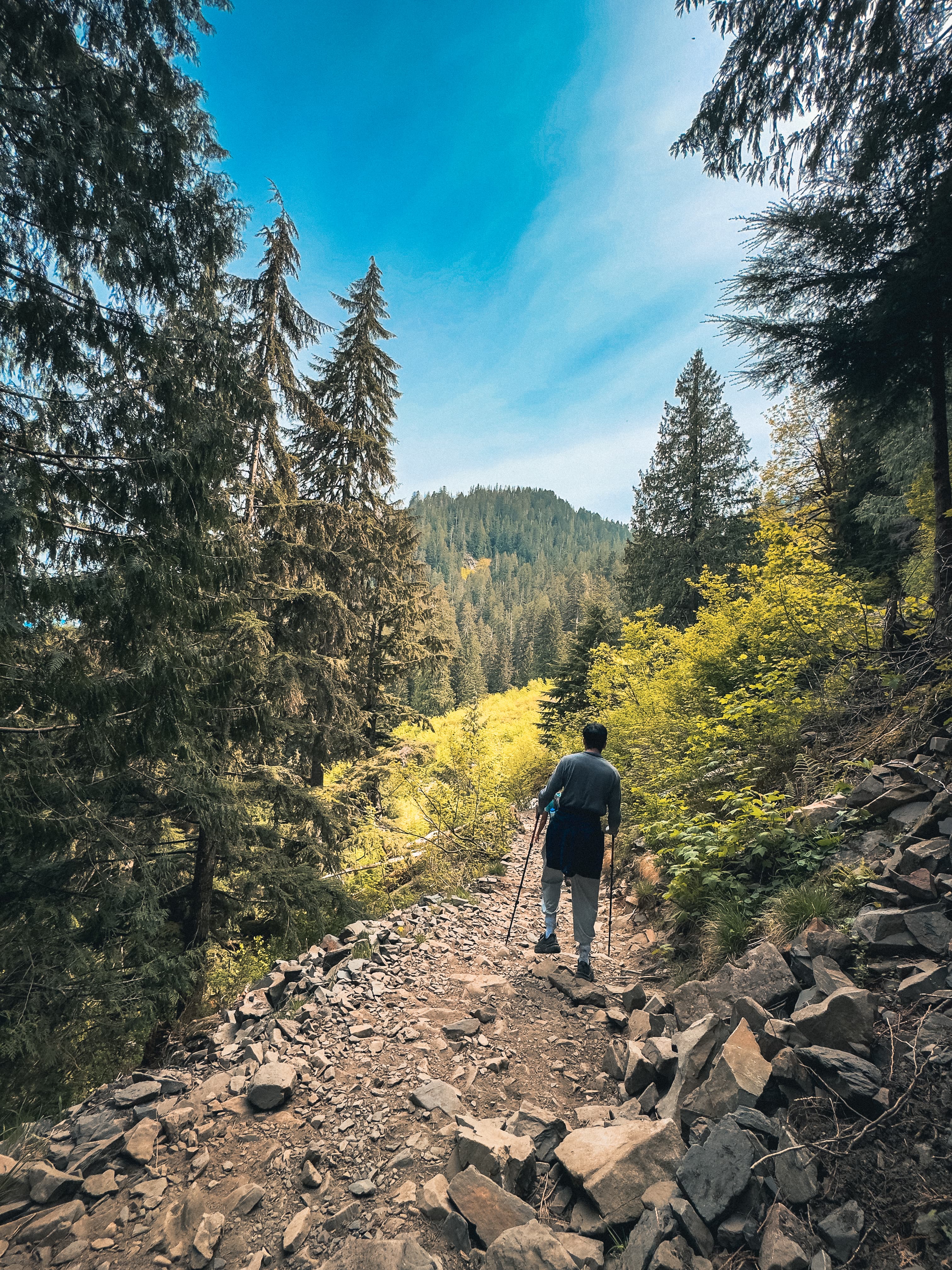 Hiker with trekking poles on rocky descent with mountain views ahead