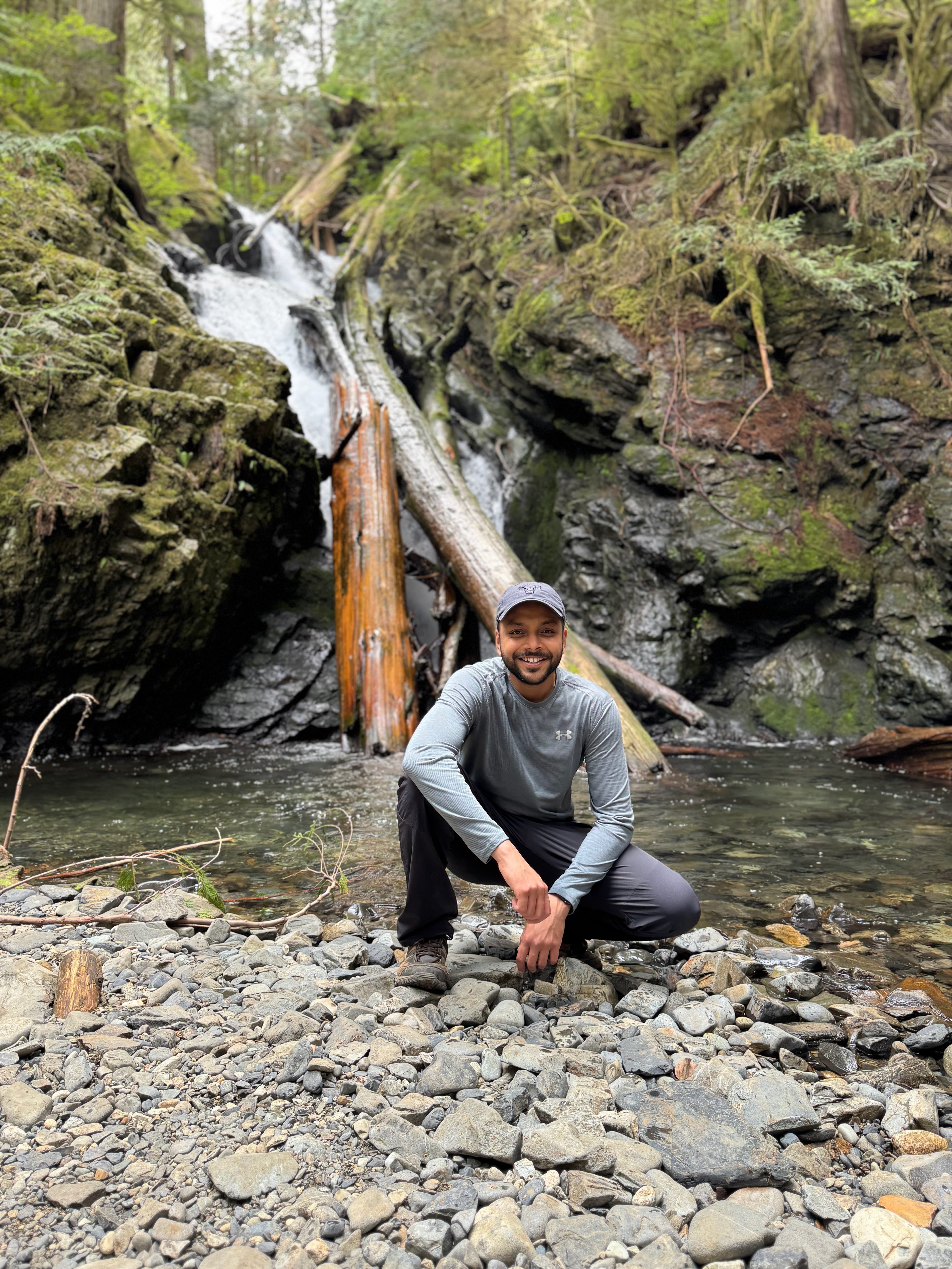 Arjun crouching on rocks at a forest waterfall